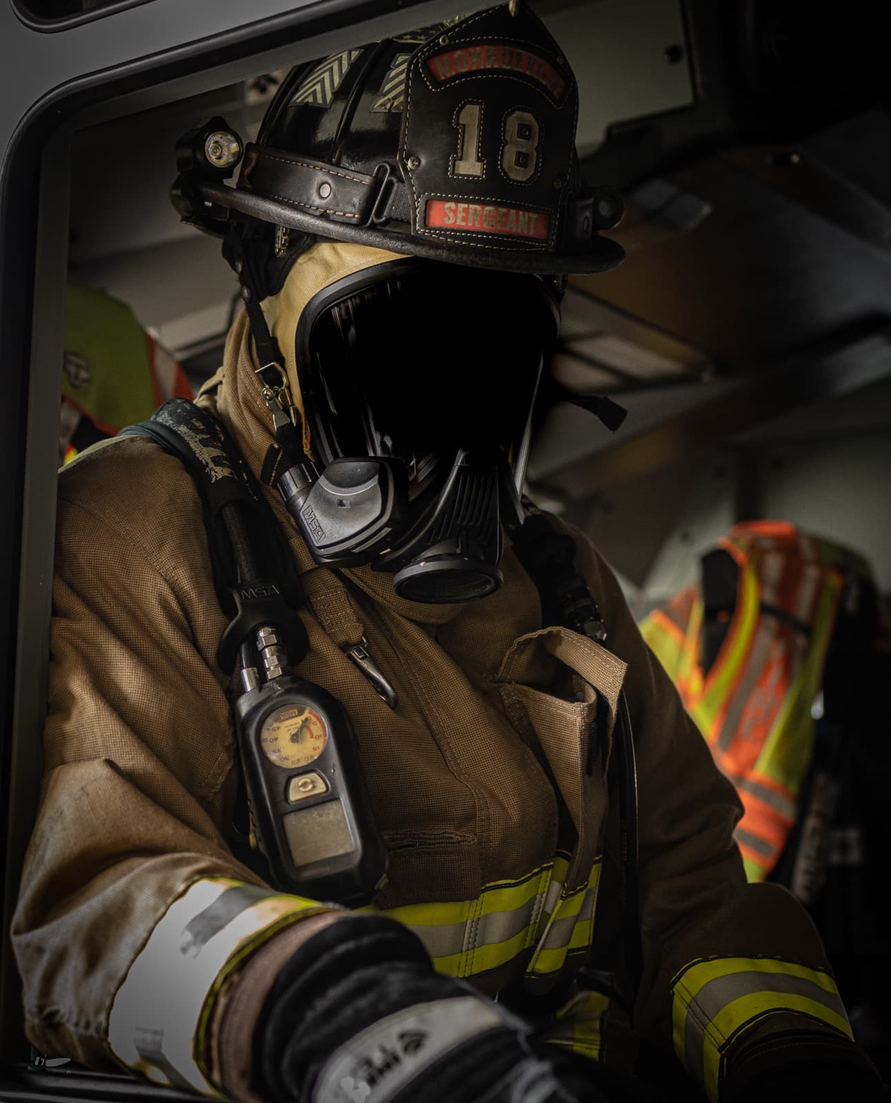 Firefighter wearing a helmet and SCBA mask seated inside the cab of an apparatus